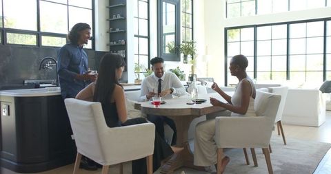 Friends chatting and sharing drinks around wooden table in bright modern dining room