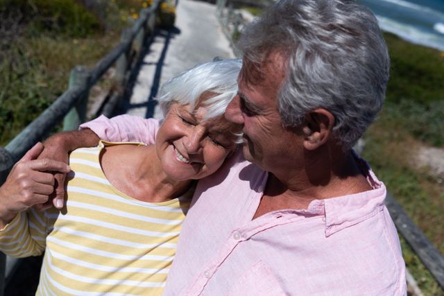 Senior caucasian couple hugging embracing each other on bridge near the beach. travel vacation retirement lifestyle concept