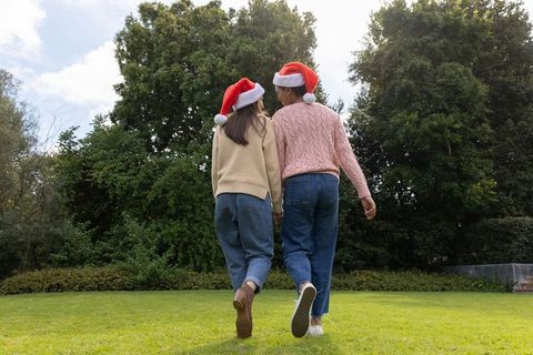 Friends walking hand-in-hand wearing santa hats on green lawn celebrating holiday togetherness