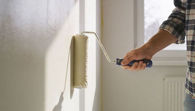 Man painting interior wall with roller applying beige paint during home renovation