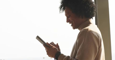 African american man using tablet by window in turtleneck, backlit business profile