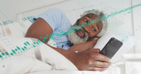 Senior man lying in bed holding smartphone watching screen with green waveform overlay