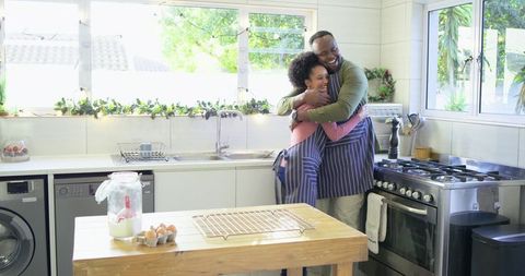 Middle-aged couple embracing while baking at bright kitchen island, joyful moment