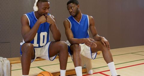Two basketball teammates discussing strategy on bench wearing blue jerseys