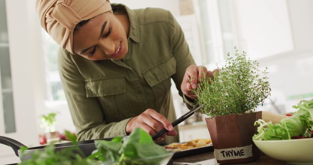 Image of happy biracial woman in hijab taking care of plants. Lifestyle, houseplants, spending free time at home concept.