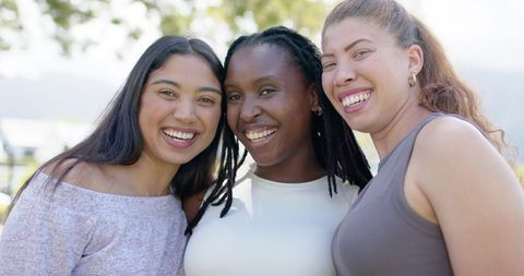 Smiling diverse friends embracing in sunny park near water, casual tops, natural light