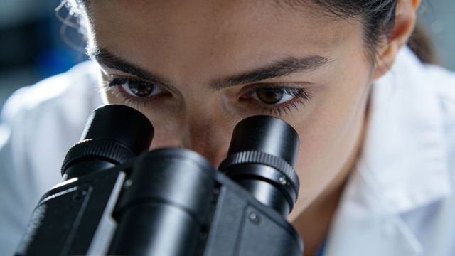 Female scientist peering through microscope eyepieces, closeup microscopy focus in lab