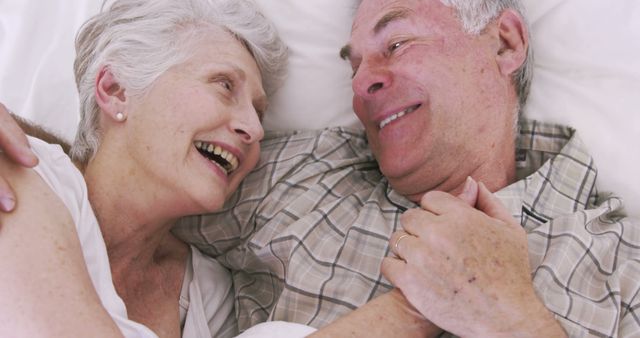 Senior couple enjoying a tender moment together while lying in bed. Both are dressed in comfortable, casual clothing and appear content and happy. Great for use in campaigns and ads targeting senior care, health and wellness brands, family connections, and lifestyle content emphasizing relationships and happiness.