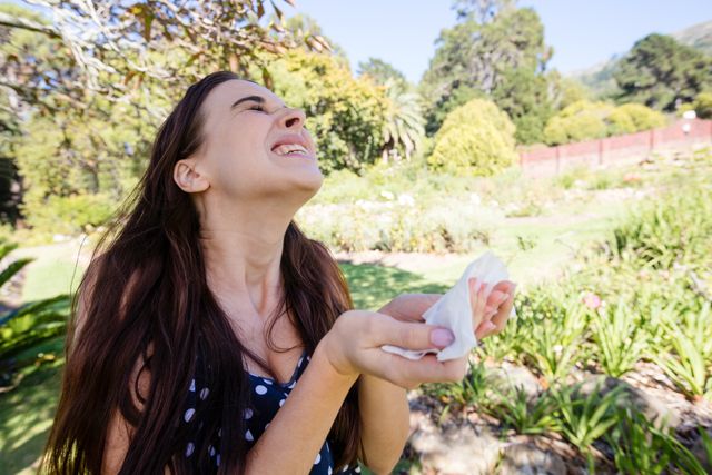 Woman sneezing holding a tissue in park