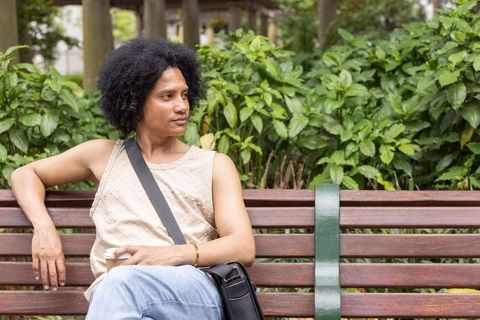 Relaxing on park bench: african american man sitting with coffee cup and messenger bag