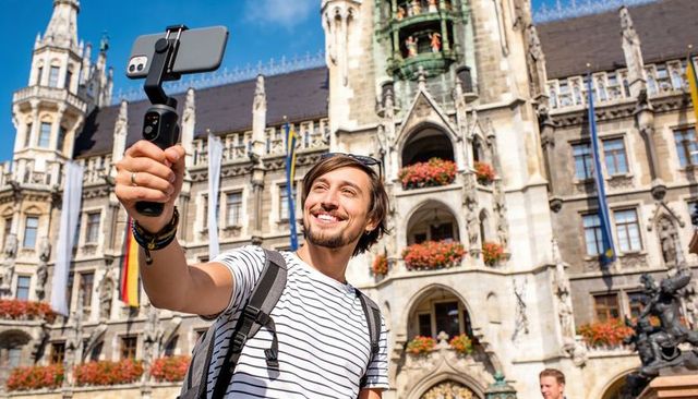 Young traveler vlogging with smartphone gimbal in urban gothic town square, smiling selfie