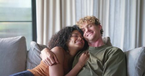 Young couple cuddling on sofa, sharing warm relaxed at-home moment of affection