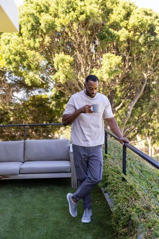 Mature african man enjoying coffee on sunlit balcony with sofa and planter
