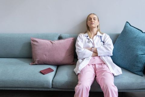 Female clinician resting on sofa in clinic lounge wearing pink scrubs and white coat