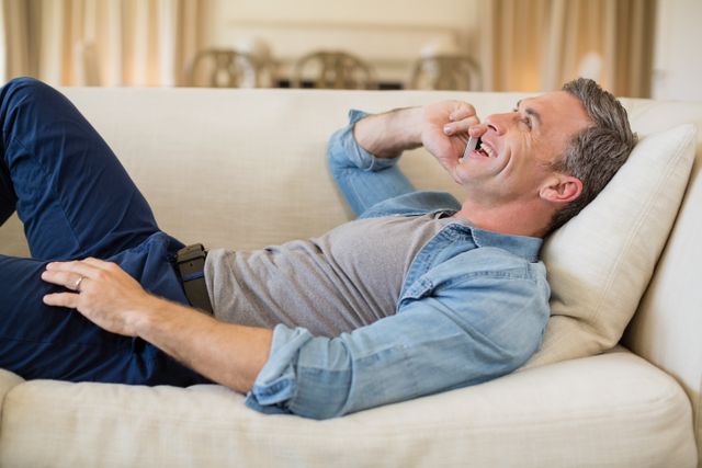 Smiling man talking on mobile phone in living room at home