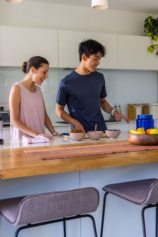 Mixed-race couple preparing healthy breakfast at wooden island in bright modern kitchen