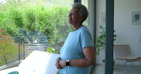 Senior african american woman standing on sunlit balcony wearing smartwatch enjoying view