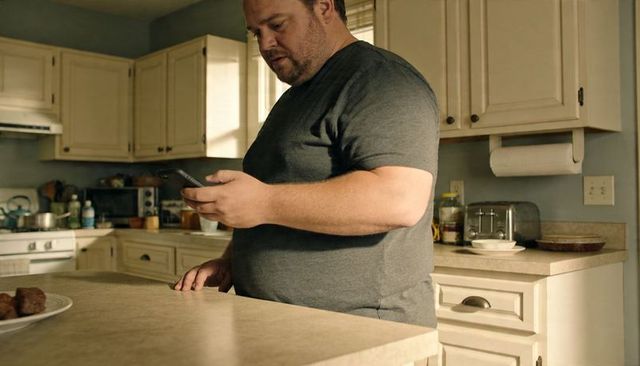 Man standing at kitchen island checking smartphone in sunlit home interior, casual domestic moment
