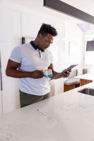 African american man standing at modern kitchen island holding mug reading clipboard