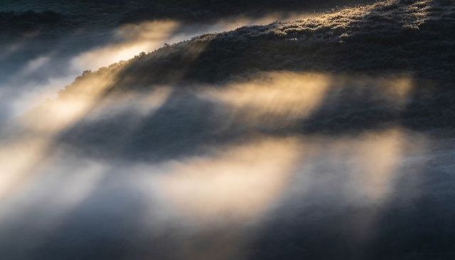 Sunlit ridge casting amber bands of fog over misty moorland and shadowed upland valley