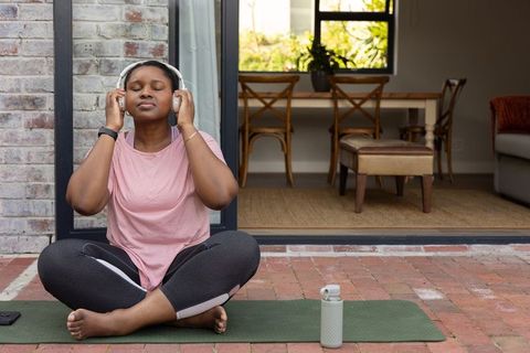 African american woman meditating with headphones on patio yoga mat practicing mindfulness