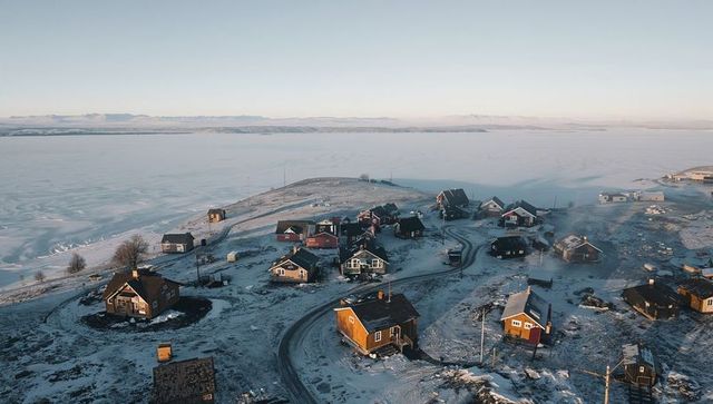 Sunrise illuminating wooden coastal village on snow-dusted shore overlooking frozen bay