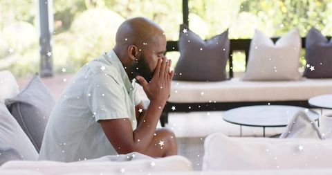 Mature man sitting contemplating on sunroom sofa, pensive solitude on sunlit patio with coffee table