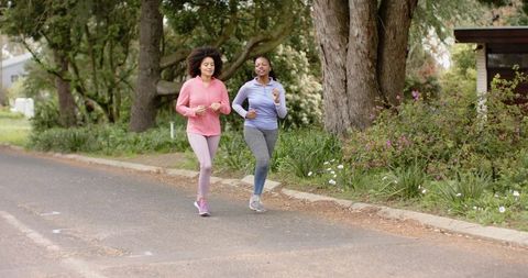 Diverse female friends jogging together on suburban street surrounded by trees and flowers