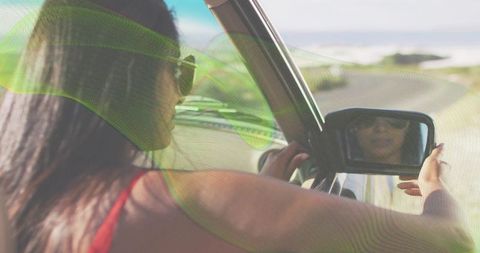 Adjusting indian woman driving convertible checking side mirror on sunlit coastal road