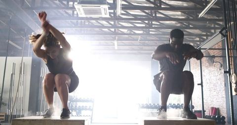 Energetic workout duo doing box jumps in crossfit gym