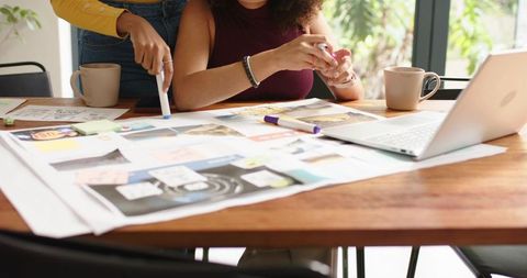 Diverse women collaborating over moodboard and laptop, brainstorming creative design layout