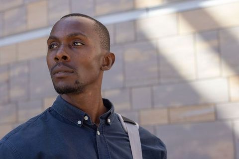 Thoughtful young african man looking upward with shoulder strap against sunlit stone facade