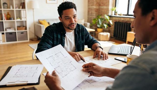 Architect discussing floor plans with consultant in bright loft home office for renovation