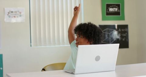 African American teen raising hand using laptop in classroom showing active learning