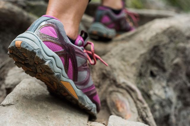 Close-up of a female hiker's foot wearing athletic shoes on a rocky trail in a forest. Ideal for use in content related to outdoor activities, hiking, fitness, adventure travel, and nature exploration.
