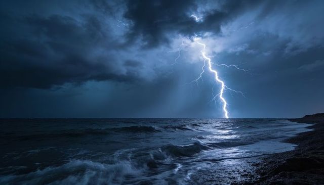 Jagged lightning bolt striking open ocean at night over rocky shoreline reflecting flash