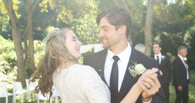 A young Caucasian bride and groom share a joyful dance outdoors, with copy space. Their wedding attire and the happiness on their faces capture a moment of celebration and love.