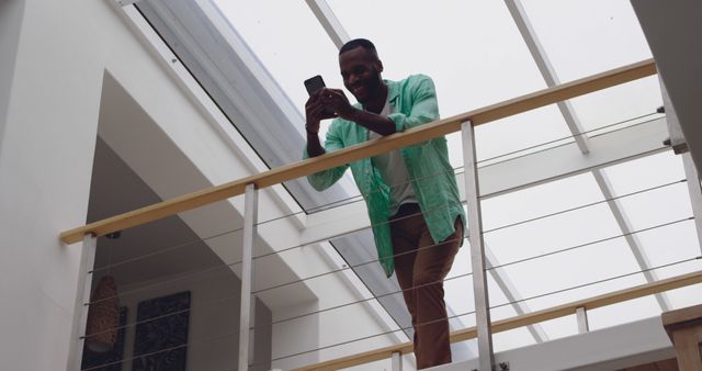 Smiling Man in Green Shirt Standing on Balcony Using Smartphone - Download Free Stock Images Pikwizard.com