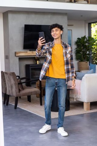 Young asian male using smartphone with earbuds in contemporary living room