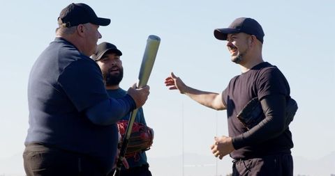 Veteran and younger players sharing laughs during casual baseball practice on sunny field