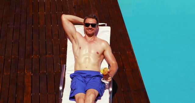 Handsome man drinking cocktail poolside on a deck chair