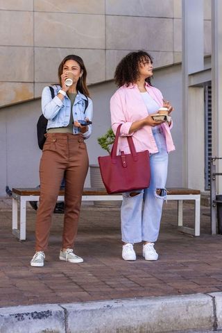 African american friends standing on urban sidewalk drinking coffee and using smartphone