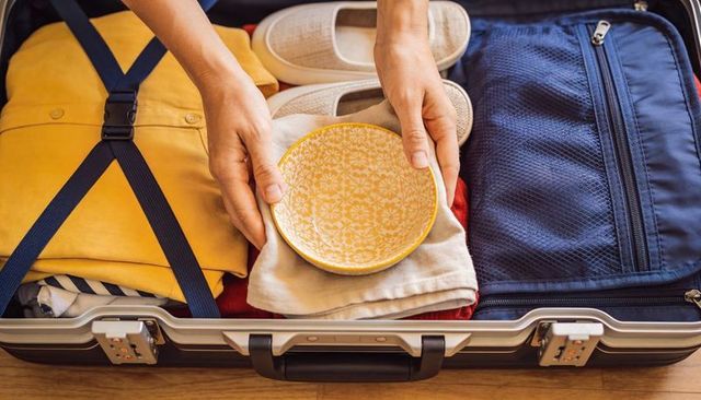 Packing delicate yellow ceramic bowl into organized hard-shell suitcase for safe travel