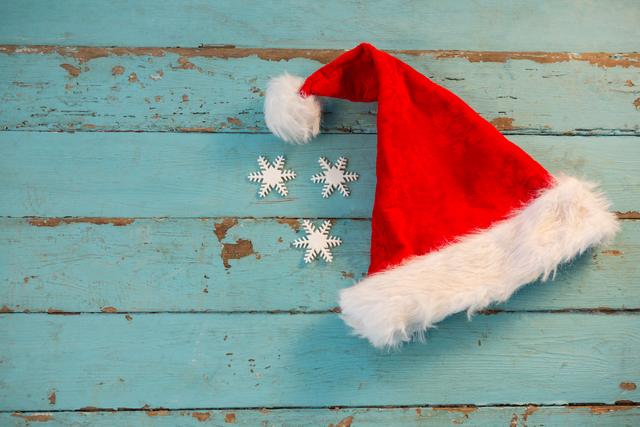 Santa hat and snowflakes on rustic wooden plank create a festive and cozy holiday atmosphere. Ideal for Christmas cards, holiday invitations, seasonal promotions, and winter-themed decorations.