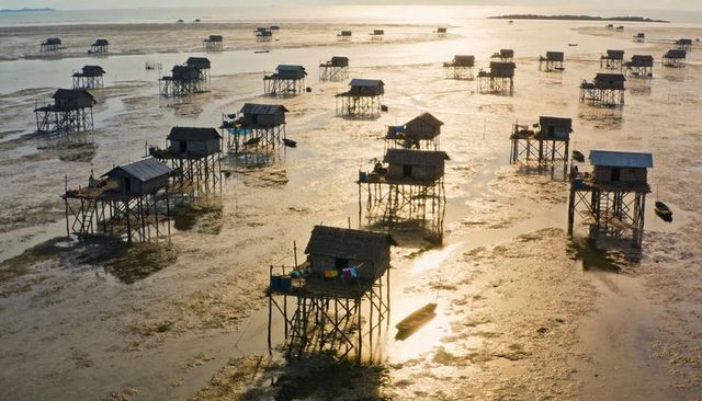 Stilt villages at low tide golden sunset over coastal mudflats with boats and laundry