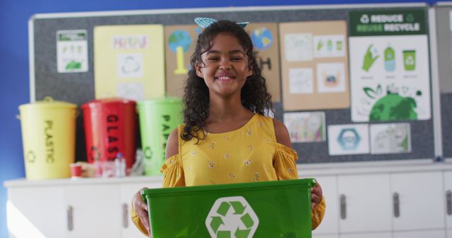 This image depicts a young girl smiling while holding a green recycling bin in a classroom environment, emphasizing educational lessons on recycling and environmental sustainability. It is suitable for use in educational materials, environmental awareness campaigns, school programs, and eco-friendly promotional content.