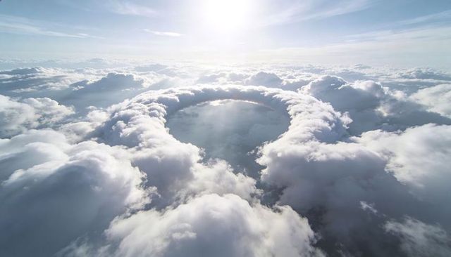Sunlit circular ring of towering cumulus clouds creating dramatic sky vortex