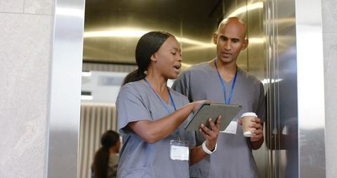 African american nurses collaborating on tablet in hospital elevator during shift handoff