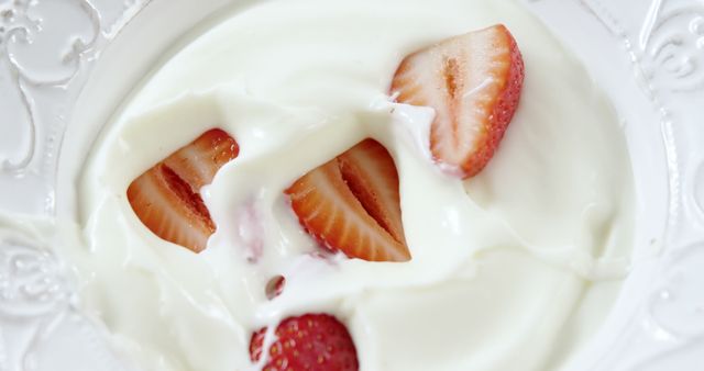 Sliced strawberries are partially submerged in creamy yogurt on a decorative white plate, with copy space. Fresh fruit like strawberries combined with yogurt is a popular choice for a healthy snack or breakfast.