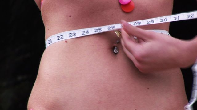 Young woman uses a tape measure to check waist size, focusing on fitness and well-being. Useful for content related to healthy living, weight loss, or personal fitness goals.